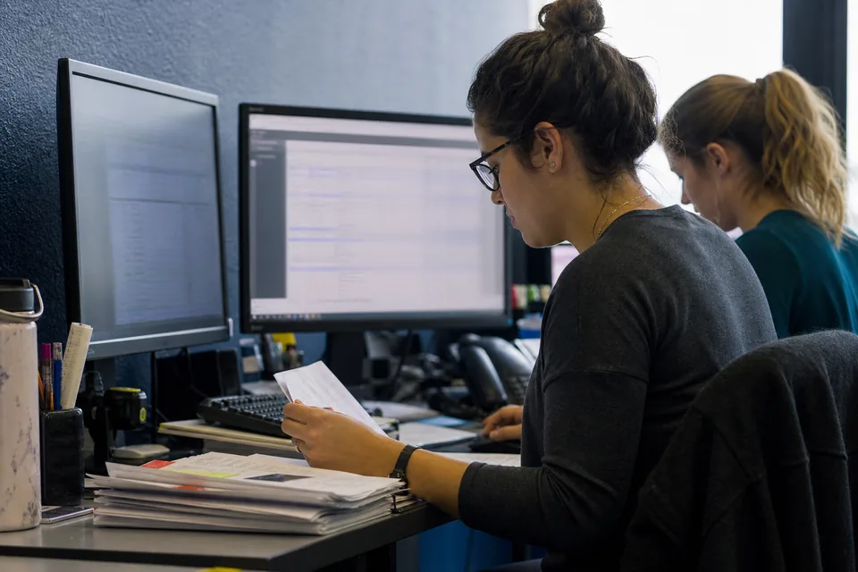 Two accounting clerks checking invoice line items on side by side monitors